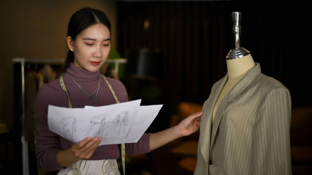 A fashion designer reviews sketches while adjusting a tailored jacket on a mannequin, blending style with activism.